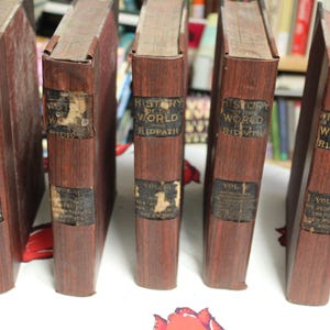 May include: A set of six brown leather-bound books with gold lettering. The books are titled "History of the World" by Ridpath. Each book has a volume number on the spine.