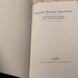 May include: An open book with a white cover and black text. The title is "Ralph Waldo Emerson Collected Poems and Translations". The book is part of "The Library of America" series.