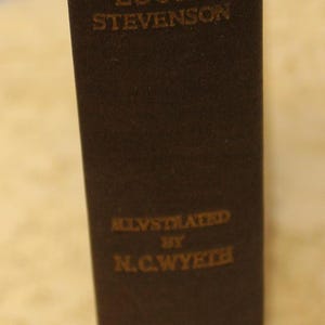 May include: A vintage hardcover book titled "The Black Arrow" by Robert Louis Stevenson, illustrated by N.C. Wyeth. The book cover is dark brown with gold lettering.