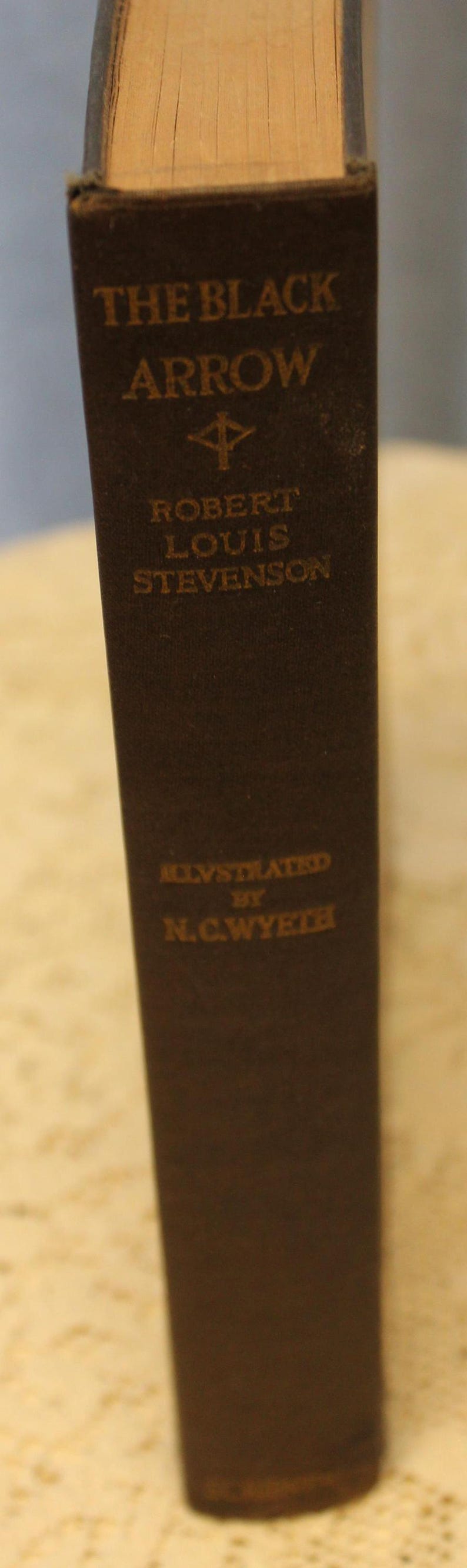 May include: A vintage hardcover book titled "The Black Arrow" by Robert Louis Stevenson, illustrated by N.C. Wyeth. The book cover is dark brown with gold lettering.