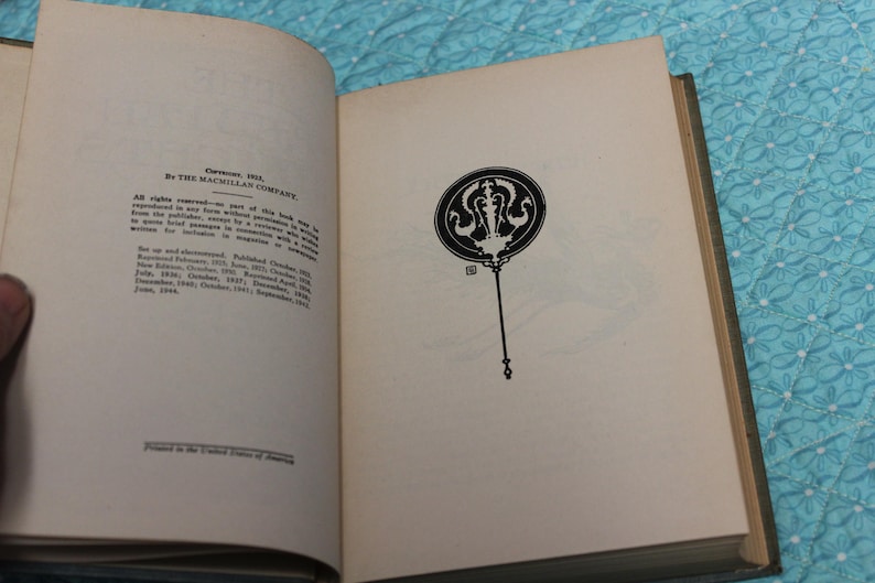 May include: Open book with text and a black and white illustration. The left page contains text about copyright and publishing information. The right page features a decorative black and white design on a long stem.