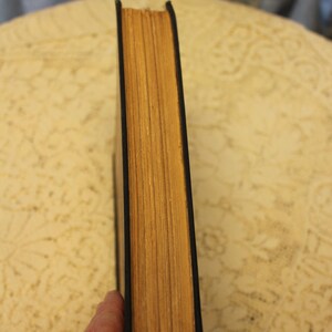 May include: The spine of a hardback book with a black cover and yellowed pages.