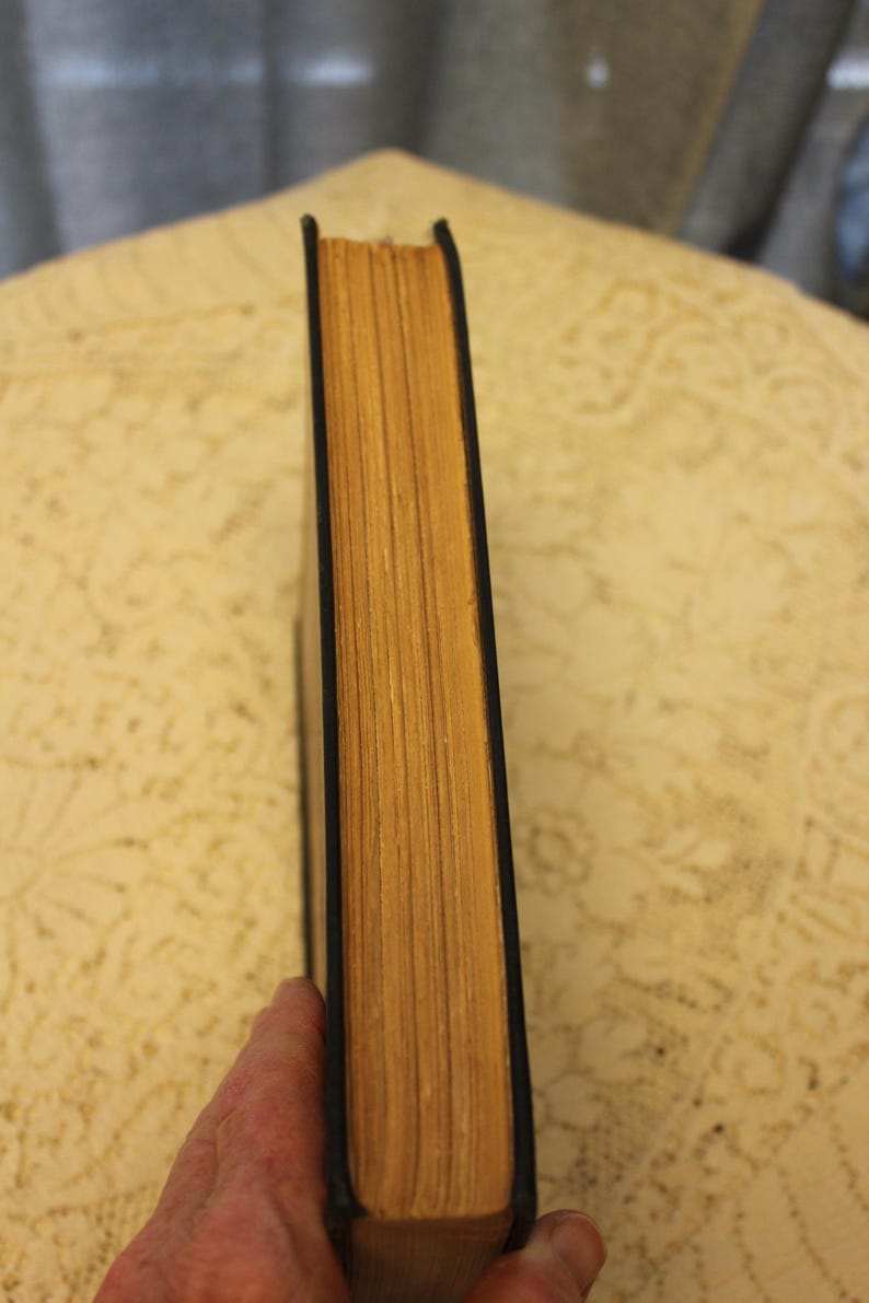 May include: The spine of a hardback book with a black cover and yellowed pages.