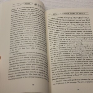 May include: A close-up of a book open to a page with text about black holes and baby universes. The text discusses the strong and weak interactions of particles and the energy required to unify them.