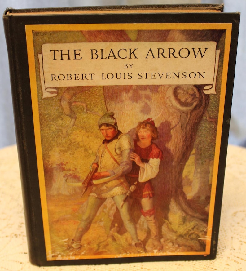 May include: The cover of a vintage book titled "The Black Arrow" by Robert Louis Stevenson. The cover features an illustration of two people in a forest setting. The people are dressed in medieval clothing and are standing near a large tree.