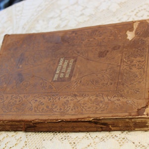 May include: A worn brown leather-bound book with the title "The Note Book of Elbert Hubbard" embossed in gold lettering. The cover features an intricate floral design.