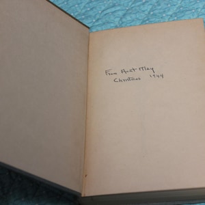 May include: Open book with aged, off-white pages and a green cover. Handwritten inscription reads "From Aunt May Christmas 1944." The book is slightly open, revealing the inscription on the right page.