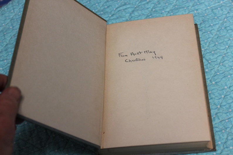 May include: Open book with aged, off-white pages and a green cover. Handwritten inscription reads "From Aunt May Christmas 1944." The book is slightly open, revealing the inscription on the right page.