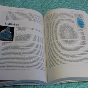 May include: An open book with text and images. One image shows a blue gemstone labeled "Larimar." The text describes the gemstone's properties and uses. The book is open on a patterned surface.
