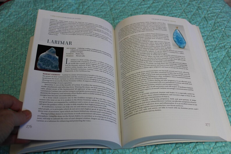 May include: An open book with text and images. One image shows a blue gemstone labeled "Larimar." The text describes the gemstone's properties and uses. The book is open on a patterned surface.