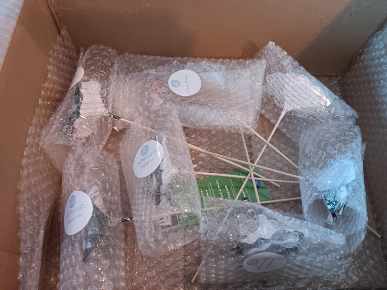 May include: A cardboard box containing several items wrapped in bubble wrap. The items, possibly decorations for an event, are secured with wooden sticks. Each item is sealed with a round sticker, suggesting a branded product.