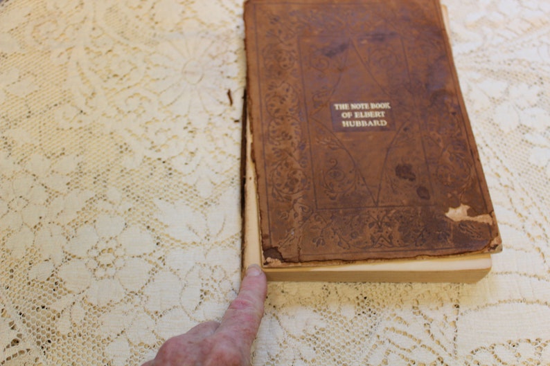 May include: The front cover of a brown leather-bound book with gold lettering that reads "The Note Book of Elbert Hubbard".
