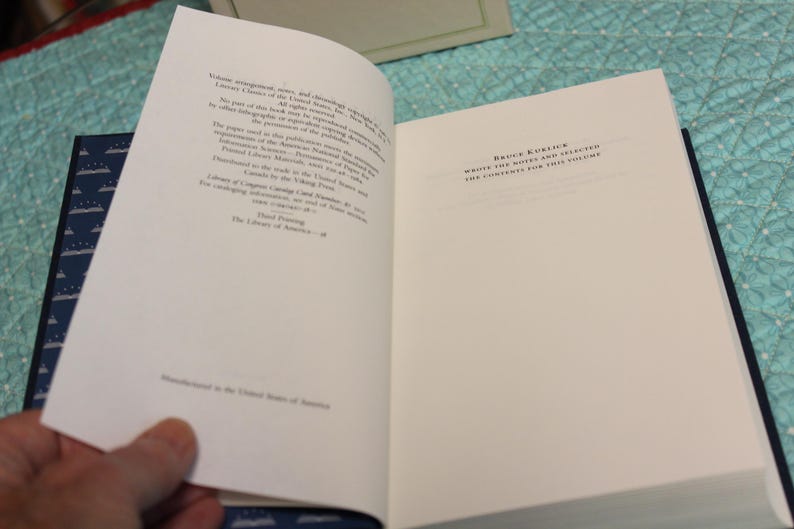 May include: An open hardcover book with white pages showing copyright and publication information on the left and the text 'Bruce Kuklick wrote the notes and selected the contents for this volume' on the right. The book has a dark blue endpaper.