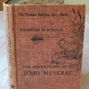 May include: A vintage book titled "The Adventures of Jerry Muskrat" by Thornton W. Burgess. The cover is a textured, reddish-brown with black text and illustrations. The book is part of "The Famous Bedtime Story Books" series.