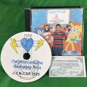 May include: A CD case and disc featuring artwork and text. The CD case displays the title "CHRISTIAN & THE HEDGEHOG BOYS" and a drawing of a person and cartoon characters. The disc has a blue heart and lightning bolts design with the text "Christian and the Hedgehog Boys". A certificate is also included.