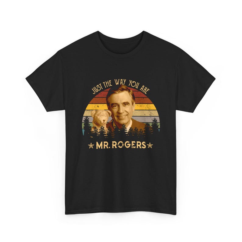 May include: A black short-sleeve t-shirt featuring a graphic of Mr. Rogers and a small puppet. The design includes a sunset background with horizontal stripes, a forest silhouette, and the text "JUST THE WAY YOU ARE" and "MR. ROGERS".