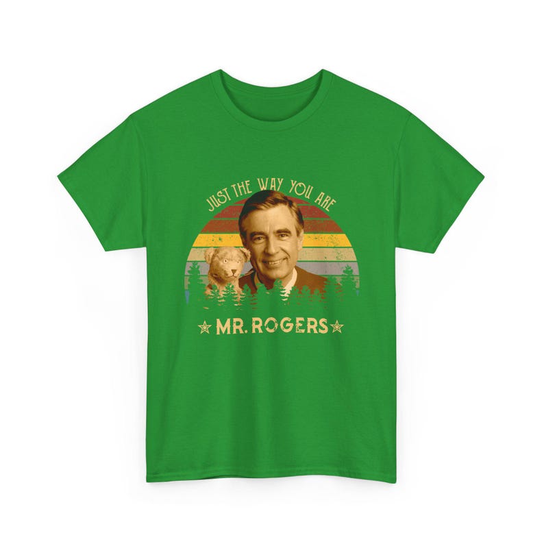 May include: A bright green short-sleeve t-shirt featuring a graphic of Mr. Rogers and a puppet. The design includes a sunset background with pine trees and the text "JUST THE WAY YOU ARE" and "MR. ROGERS" printed in a retro-style font.