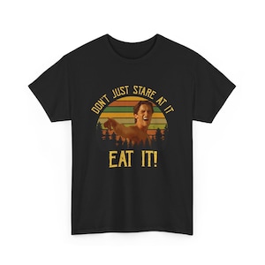 May include: Black t-shirt with a graphic of a man pointing, set against a sunset backdrop with trees. The text reads "DON'T JUST STARE AT IT" above and "EAT IT!" below the image.