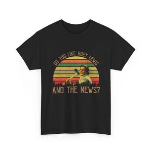 May include: Black t-shirt featuring a retro design with the text "DO YOU LIKE HUEY LEWIS AND THE NEWS?" above an image of a man holding an axe. The design includes a sunset with green, yellow, orange, and red stripes.