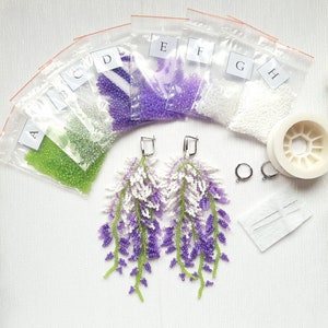 May include: A kit for making beaded earrings featuring a wisteria flower design. The kit includes bags of purple, white, and green beads, a spool of beading thread, two earring hooks, and two needle threaders.