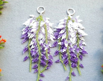 May include: A pair of dangle earrings with a beaded design that resembles wisteria flowers. The earrings are made with white, purple, and green beads.