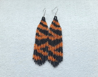 May include: A pair of long, beaded earrings with a black and orange tiger stripe pattern.
