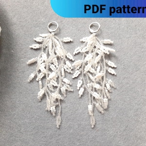 Könnte beinhalten: Ein Paar lange, weiße Perlenohrringe mit einem zarten, floralen Design. Die Ohrringe sind aus kleinen, weißen Perlen gefertigt und haben einen silbernen Hakenverschluss.