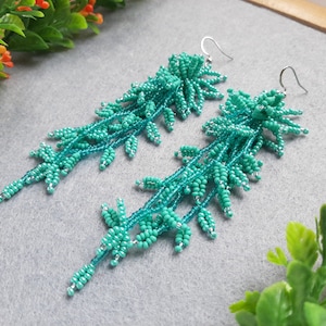 May include: A pair of long, turquoise beaded earrings with a leafy design. The earrings are made with small, round beads and have a delicate, feminine look.