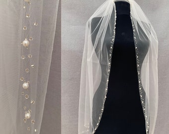 May include: A white tulle wedding veil with a beaded trim. The veil is decorated with small pearl-like beads.