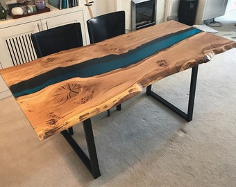May include: A handcrafted wooden table with a live edge design. The table features a river of teal-colored epoxy resin running down the center. The wood has a natural, light brown color and is supported by black metal legs.