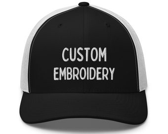 May include: A black and white trucker hat with a black crown and a white mesh back. The hat has the text "CUSTOM EMBROIDERY" embroidered in white on the front.