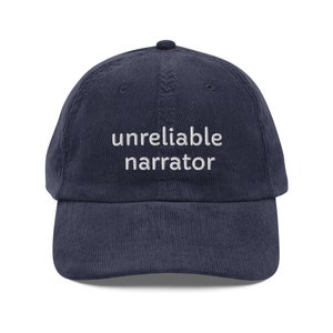 May include: A navy blue corduroy baseball cap with white embroidered text that reads "unreliable narrator".