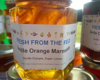 May include: A glass jar of Seville orange marmalade with a white label that reads "FRESH FROM THE FIELD Seville Orange Marmalade Seville Oranges, Sugar, Lemon".