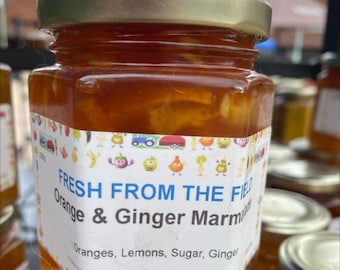 May include: A glass jar of orange and ginger marmalade with a colorful label that says "FRESH FROM THE FIELD Orange & Ginger Marmalade" and lists the ingredients: Oranges, Lemons, Sugar, Ginger. The label also includes the maker's address: Bishops Waltham, Southampton Hants SO32 1FP.