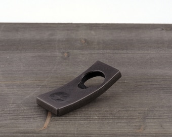 May include: A black metal bottle opener with a curved design. The opener has a circular hole for opening bottles.