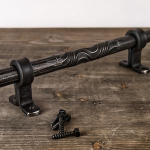 May include: Black metal door handle with a wavy design and two mounting brackets. The handle is shown on a wooden surface with four black screws.