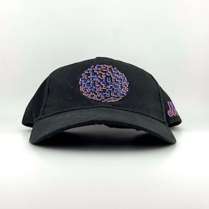 May include: A black baseball cap featuring an embroidered circular graphic on the front composed of small blue and orange squares. The side of the cap displays the text "METS" in blue lettering with an orange outline, stitched in a bold font.