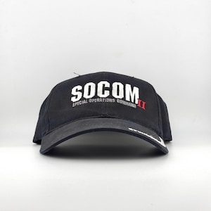 Puede incluir: Gorra de béisbol negra con la palabra "SOCOM" en letras blancas. Debajo, el texto "SPECIAL OPERATIONS COMMAND" también en blanco. El número romano "II" es rojo. La visera es de color gris oscuro.