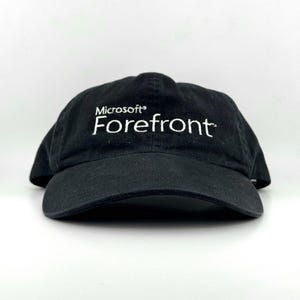 May include: A black baseball cap featuring the white embroidered text Microsoft Forefront on the front panel. The cap has a structured crown, a curved brim, and a classic six-panel design with stitched eyelets for ventilation and a fabric strap.