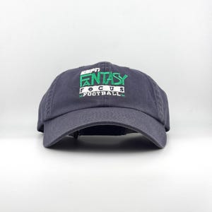 May include: A navy blue baseball cap with the text "ESPN FANTASY FOCUS FOOTBALL" embroidered in green and white. The cap has a curved brim and an adjustable strap.