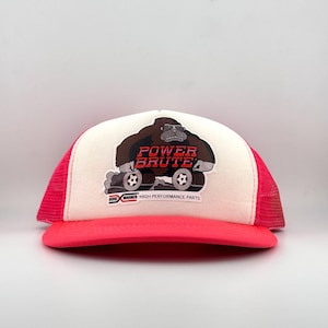 May include: A trucker hat with a white front panel and a bright pink brim and mesh back. The hat features a graphic of a gorilla with the words "POWER BRUTE" in red and the text "BORG WARNER HIGH PERFORMANCE PARTS".