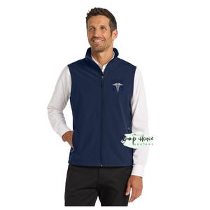 May include: Navy blue vest with a full zipper, featuring a white shirt underneath. The vest has a small embroidered design on the chest and two side pockets. The vest is a medical professional's uniform.