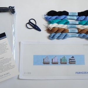 May include: A needlepoint kit featuring a rectangular canvas with four beach hut designs, six skeins of embroidery thread in black, blue, teal, white, and brown, a pair of small blue scissors, a clear zipper pouch, and a printed how-to guide.