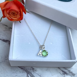May include: A silver necklace with a green gemstone and a silver letter 'A' charm. The necklace is in a white box with a sticker that says "Bear & Bug" and "Hand Stamped Gifts & Jewellery".