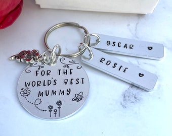 May include: A silver keyring with a round charm inscribed "FOR THE WORLD'S BEST MUMMY" with floral and butterfly motifs. Two rectangular tags are engraved with the names "OSCAR" and "ROSIE". A red flower charm is attached.