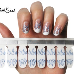 May include: A sheet of blue and white nail wraps with a flame design. The nail wraps are shown on a hand with a white base coat and blue flame design.