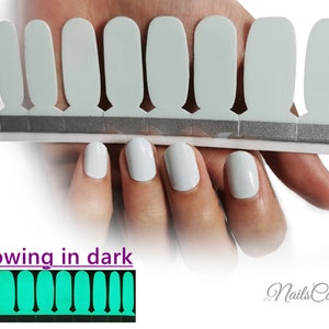 May include: A set of 10 white nail wraps that glow in the dark. The wraps are shown on a hand with white nail polish. The wraps glow a bright green in the dark. The text "Nails Cool" is visible in the image.