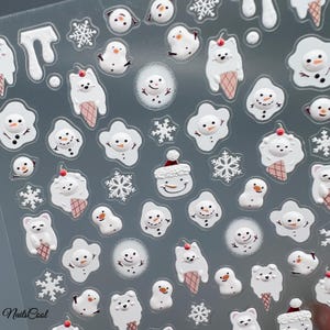 May include: A sheet of nail art stickers featuring winter-themed designs. The stickers include white snowmen, snowflakes, and polar bears with ice cream cones. The designs are in white, red, and brown, with a clear background. The text "Nails Cool" is visible in the bottom left corner.