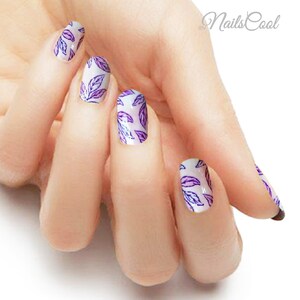 May include: A hand model wearing nail wraps with a white background and a purple and white leaf design. The nail wraps are from Nails Cool.