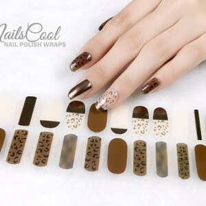 May include: A set of brown and gold leopard print nail polish wraps. The wraps are designed to be applied to fingernails. The image shows a hand wearing the nail wraps.